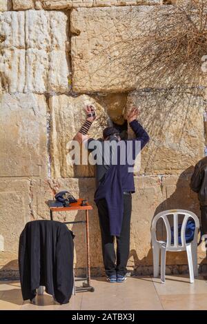 Gerusalemme, Israele - 19 febbraio 2017: Un uomo non identificato prega e mette le sue mani sul Muro Occidentale, il luogo più sacro per il giudaismo, in una giornata di sole. Foto Stock