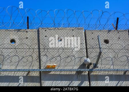 Un primo piano del muro grigio di separazione del cemento tra Israele e Palestina. Una palla e una bottiglia da bambini nella West Bank catturati nel filo spinato Foto Stock