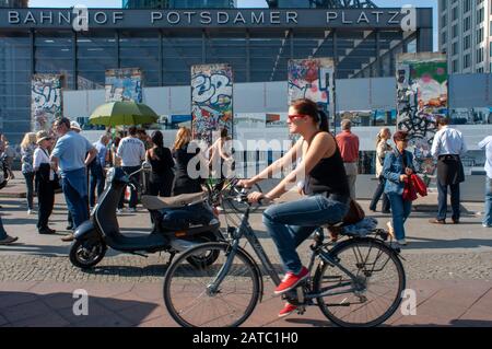 Turisti in bicicletta presso le sezioni originali del muro di Berlino a Potsdamer Platz a Berlino Germania Foto Stock