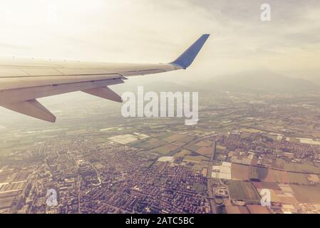 Ala di un aereo che vola sopra città e villaggi. L'ala dell'aereo sullo sfondo del cielo e della terra. Veduta aerea panoramica della terra di motley da airpl Foto Stock