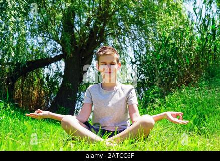 Un ragazzo siede su un prato verde in posizione loto e medita Foto Stock