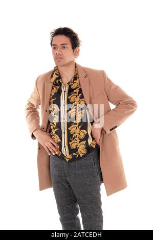 Un bel ragazzo alto che si alza con le mani sui fianchi in un cappotto beige che guarda lontano, isolato per sfondo bianco Foto Stock