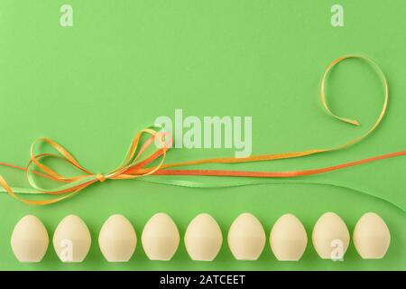 Pasqua ancora vita. Uova di cioccolato bianco e nastri colorati sullo sfondo verde. Spazio di copia. Foto Stock