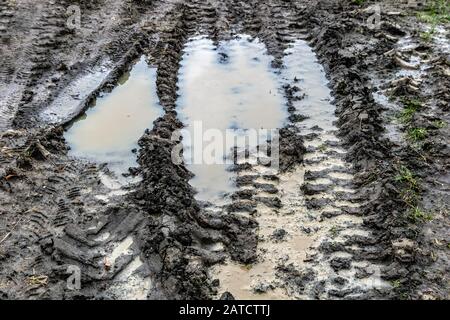 Un cantiere con tracce di auto nel fango. Tracce di carrelli nel fango. Fangoso con pozzanghere. Foto Stock