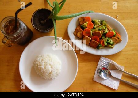 Vista dall'alto del tofu saltato in padella e delle verdure, riso bianco al vapore e caffè freddo, sano pasto vegano a base vegetale Foto Stock