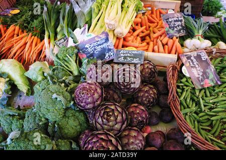 Verdure fresche coltivate localmente, carciofi, piselli, carote e scalogni in vendita al mercato di strada francese all'aperto di le Bois-d'Oingt Foto Stock