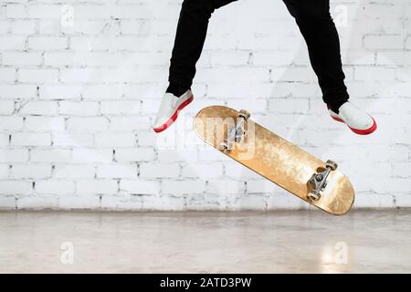 Skateboarder esecuzione skateboard trucco - kick flip su cemento. Atleta olimpico che pratica salto su sfondo bianco, preparazione per la concorrenza. Extr Foto Stock