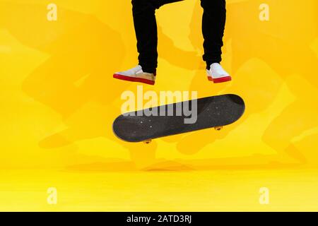 Skateboarder esecuzione skateboard trucco - kick flip su cemento. Atleta olimpico che pratica salto su sfondo giallo in studio, in preparazione per la co Foto Stock