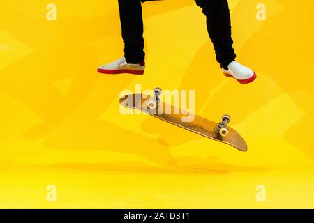 Skateboarder esecuzione skateboard trucco - kick flip su cemento. Atleta olimpico che pratica salto su sfondo giallo in studio, in preparazione per la co Foto Stock