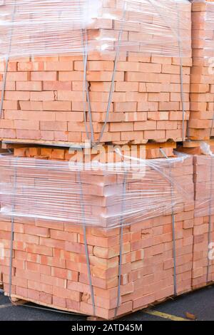 Diversi pallet con mattoni di cemento sovrapposti in magazzino. La produzione industriale di mattoni. foto verticale. Foto Stock