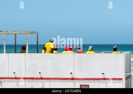 Bagnini, salvavita in servizio nella loro torre sulla spiaggia di Muizenberg, Cape Peninsula, Sudafrica indossando giallo e rosso uniforme concetto di sicurezza pubblica Foto Stock