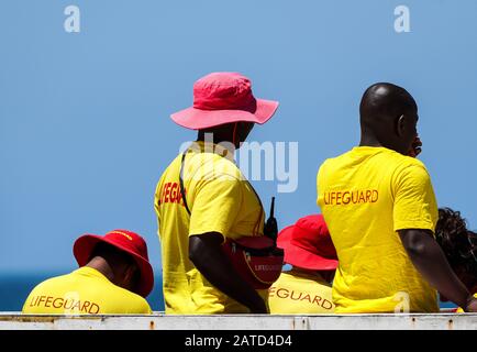 Tessitori, bagnini in servizio indossando uniforme gialla e rossa alla loro torre alla spiaggia di Muizenberg, Cape Peninsula, concetto di sicurezza pubblica del Sudafrica Foto Stock