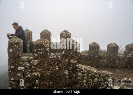 Sintra, Portogallo - 18 Gennaio 2020: L'uomo del turismo cerca di scattare foto al Castello Moresco durante una giornata molto nebbiosa con scarsa visibilità Foto Stock