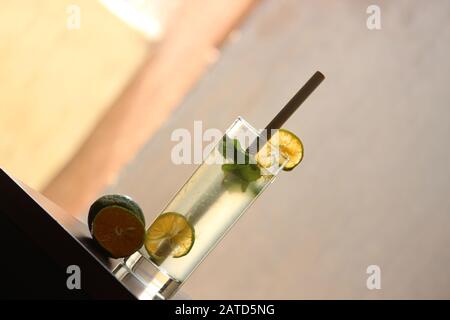 Limonata soda in Tall vetro con cannuccia di bambù con foglie di menta e limoni freschi tagliati sullo sfondo Foto Stock