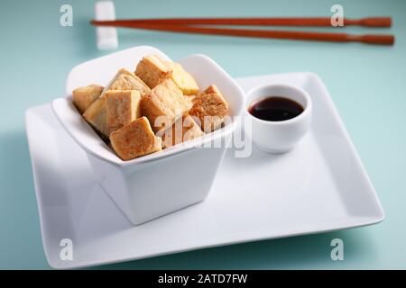 Tofu fritto servito con salsa di soia su un piatto bianco di primo piano Foto Stock