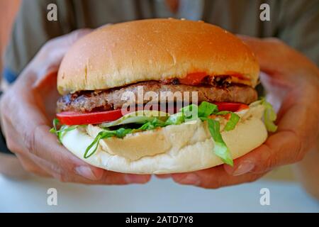 Un gustoso e grande hamburger tenuto in mano Foto Stock