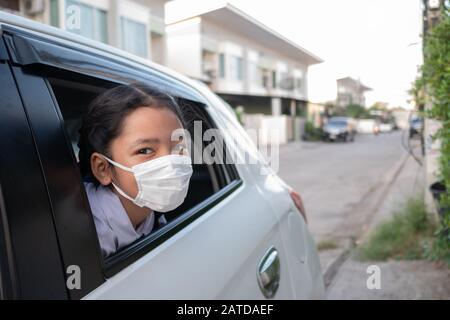 Un bambino che indossa una maschera igienica ha schioccato la testa fuori dal finestrino dell'auto. Foto Stock