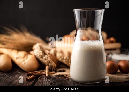 Latte in una bottiglia di vetro poste su di un tavolo di legno con gli ingredienti per la produzione di pane e prodotti da forno Foto Stock