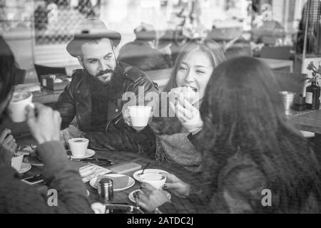 Amici felici che mangiano la colazione e bevono caffè con latte nella caffetteria del bar - Vista attraverso il vetro con riflessione - montaggio in bianco e nero - Focus o Foto Stock