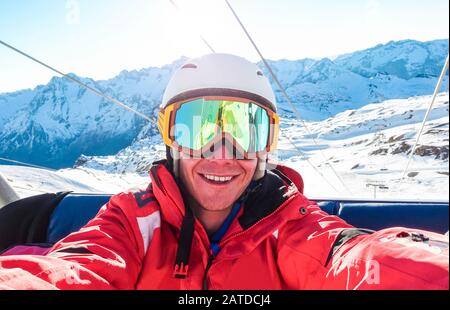 Felice snowboarder scattare foto selfie con fotocamera smartphone seduta su skilift - giovane uomo divertirsi in vacanza neve inverno resort - sport estremo Foto Stock