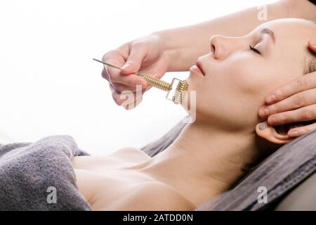 Scorrimento del viso contro il mento durante il massaggio viso di gua sha presso la clinica di bellezza. Foto Stock