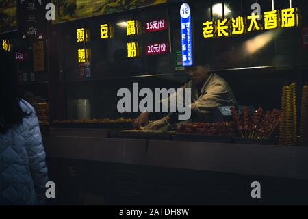 Pechino, Cina - 26 Dicembre 2018: Stand Gastronomico A Wangfujing Street. Una cameriera che vende cibo di strada tradizionale cinese. Foto Stock