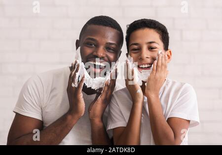 Felice Afro Padre E Suo Figlio Con Schiuma Da Barba Sulle Facce Foto Stock