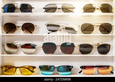 Occhiali da sole di diversi colori sul banco bianco del negozio. Bello e luminoso, selezione e assortimento, bagliore solare sul bancone Foto Stock