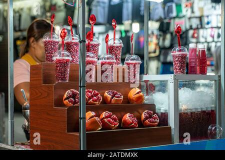 Melograno sbucciato e succo di melograno sulla strada della Thailandia. Street food e succo fresco sano. Ragazza che vende semi di melograno in tazze. OUTsi Foto Stock