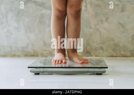 Ragazza piccola su scala del peso sullo sfondo del pavimento, concetto di dieta. Foto Stock