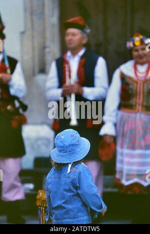 Un bambino che guarda gli artisti di strada indossando costumi nazionali, Piazza del mercato principale. Cracovia. Polonia. Europa Foto Stock