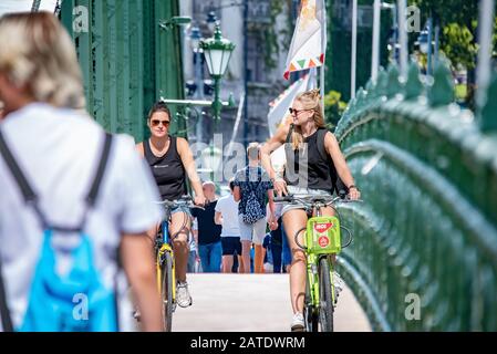 Moto millennial in una dinamica scena estiva sul Ponte della libertà a Budapest. Ragazze bionde e brunette. Foto Stock