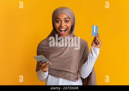 Ragazza Musulmana Nera Con Gioia In Hijab Holding Carta Di Credito E Smartphone Foto Stock