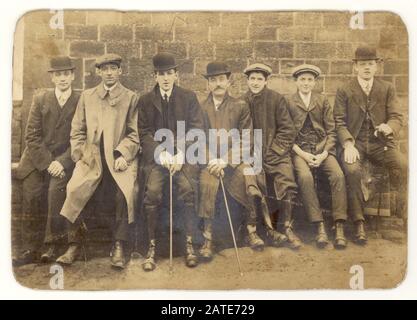 Inizio 1900's Edwardian cabinet card di gruppo di sette giovani uomini e ragazzi indossando cappelli piatti e cappelli da arco, alcuni che tengono bastoni o canne da passeggio, collari arrotondati, seduti insieme a riposo dopo una passeggiata su una panchina, Regno Unito Circa 1905 Foto Stock