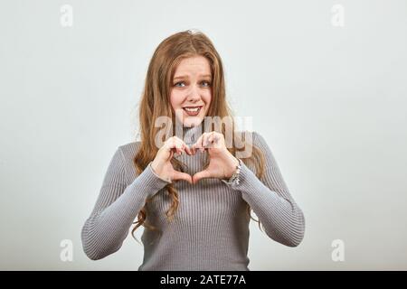 donna in grigio maglione sorride con felicità, mostrando le mani la forma del cuore Foto Stock