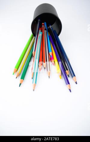 Vista dall'alto di un vaso pieno di pastelli di matita colorati caduti su uno sfondo bianco Foto Stock
