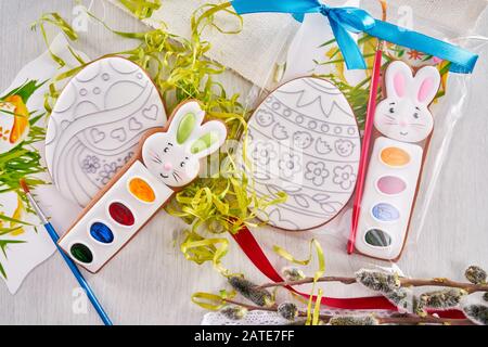 Da sopra vista di set di pittura regalo per colorare le uova di pasqua, isolato su tavola di legno. Vernici acquerello vicino a tovagliolo, erba falsa, ramo di salice e spazzole. Concetto di vacanze di primavera e pasqua. Foto Stock