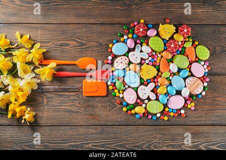 Biscotti colorati glassati allo zenzero, narcisi e palline di cioccolato con guscio di zucchero. Dolce fatto in casa di animali pasquali, uova e carote a forma di cerchio, tre utensili da cucina in silicone nelle vicinanze. Foto Stock