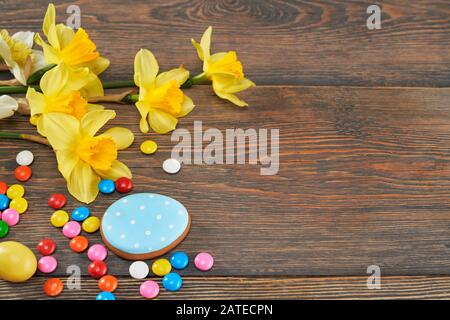 Raccolto di biscotti colorati glassati allo zenzero e palline di cioccolato e daffodils isolati su sfondo di legno. Primo piano di deliziosa pasticceria fatta in casa a forma di uova di pasqua. Concetto di vacanze. Foto Stock