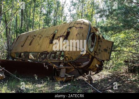 Abbandonato e rusty bus in un campo in una giornata soleggiata con cielo blu e nuvole nella centrale nucleare di Cernobyl la zona di alienazione Foto Stock