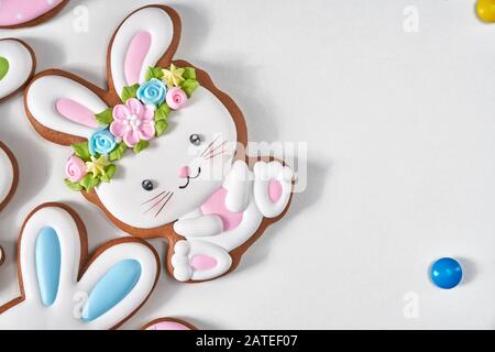 Vista dall'alto di colorati biscotti glassati allo zenzero e palline di cioccolato isolate su sfondo bianco. Primo piano di deliziosa pasticceria fatta in casa a forma di coniglio di pasqua in corona di fiori. Foto Stock