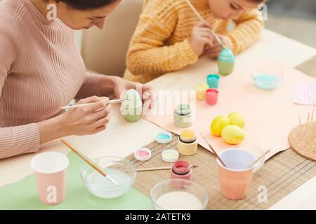 Ritratto ad alto angolo di madre e figlia pittura Pasqua uova pastello colori seduti al tavolo in accogliente cucina interno, copia spazio Foto Stock