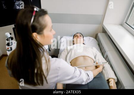 Il medico professionista sta esaminando l'addome femminile e i reni usando l'apparecchiatura di ultrasuoni. Giovane paziente caucasico donna è in esame sul ultrasuoni Foto Stock