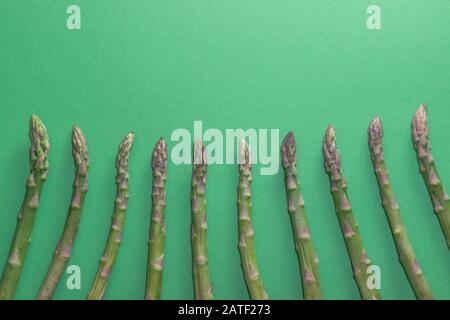 Asparagi verdi crudi e sani su sfondo verde. Concetto di detox e superfood. Foto Stock