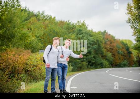 Gesto di hitchhiking. Inizia la grande avventura nella tua vita con hitchhiking. Compagnia amici viaggiatori hitchhiking a fondo natura strada. Viaggiatori sulla loro strada. Amici hitchhikers in viaggio. Foto Stock