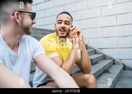 Ritratto di felice coppia gay di trascorrere del tempo insieme seduti sulle scale all'esterno. Lgbt e il concetto di amore. Foto Stock