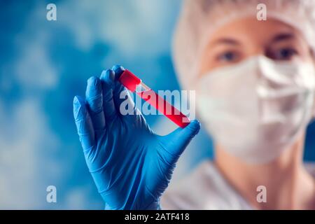 Medico in maschera medica e guanti blu in provetta con esame del sangue. Medicina e concetto di assistenza sanitaria. Foto Stock