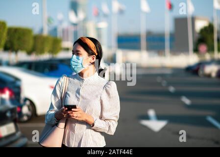 Ragazza asiatica che indossa maschera facciale in un parcheggio all'aperto Foto Stock