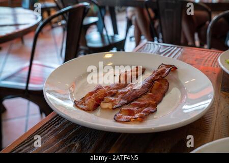 Piatto di tre fette di pancetta seduta su un piatto bianco nel ristorante Foto Stock