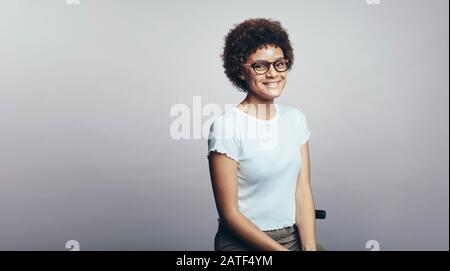 Ritratto di una giovane donna sorridente che indossa occhiali isolati su sfondo grigio. Donna d'affari sorridente con capelli ricci che guarda la macchina fotografica. Foto Stock